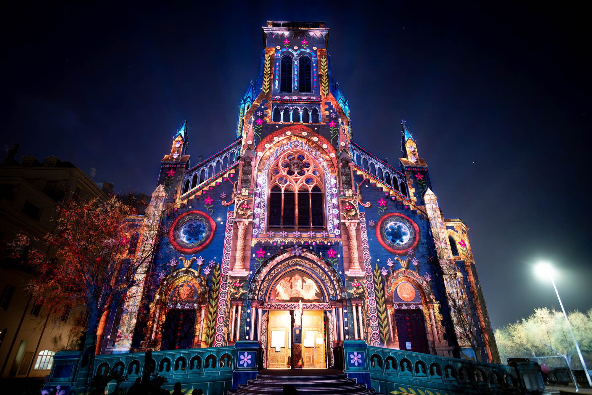 Front of an elaborately carved cathedral. Brightly glowing plant and flower imagery is projected on it.