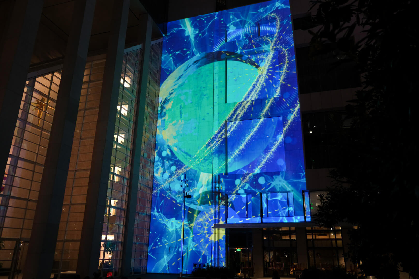 Front of a glass-walled building. Images of planets and stars projected on it.
