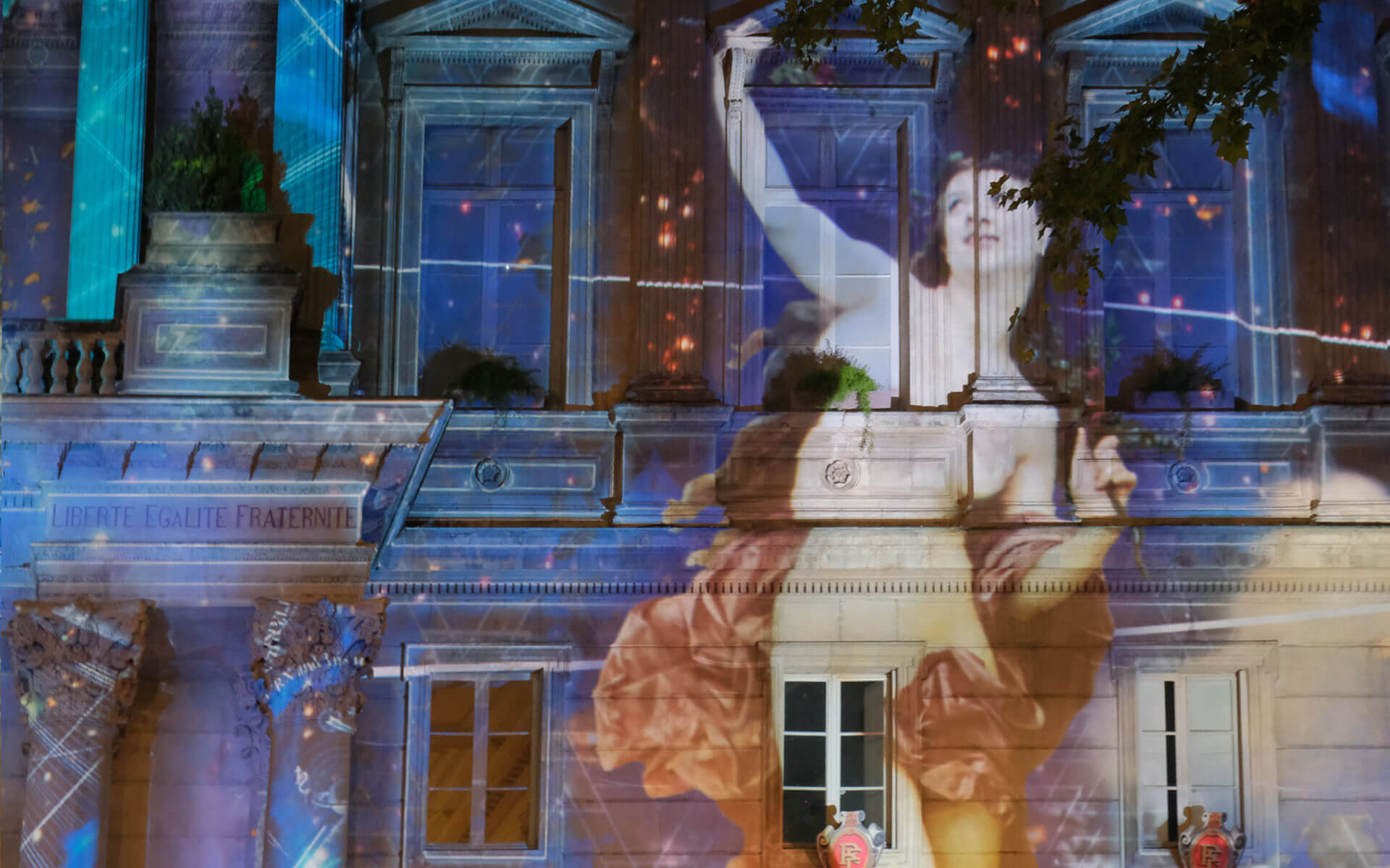 Front of an old European building with a painting of a white woman raising her arm in a dramatic gesture projected on it