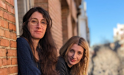 Two white women with long hair posing against a brick building