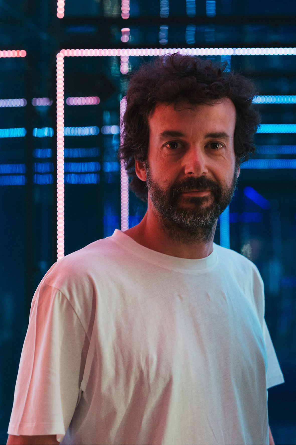 White man with a dark beard wearing a white t-shirt.