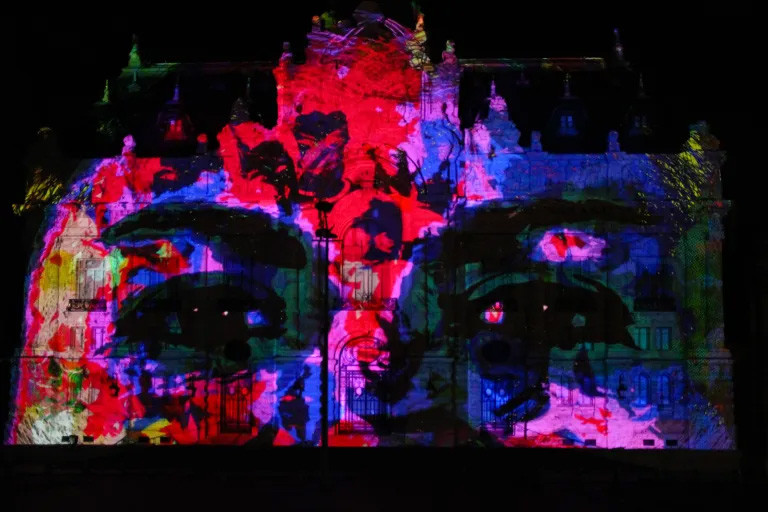 Elaborately carved and adorned building front with a neon-colored image of a person's eyes projected on it.